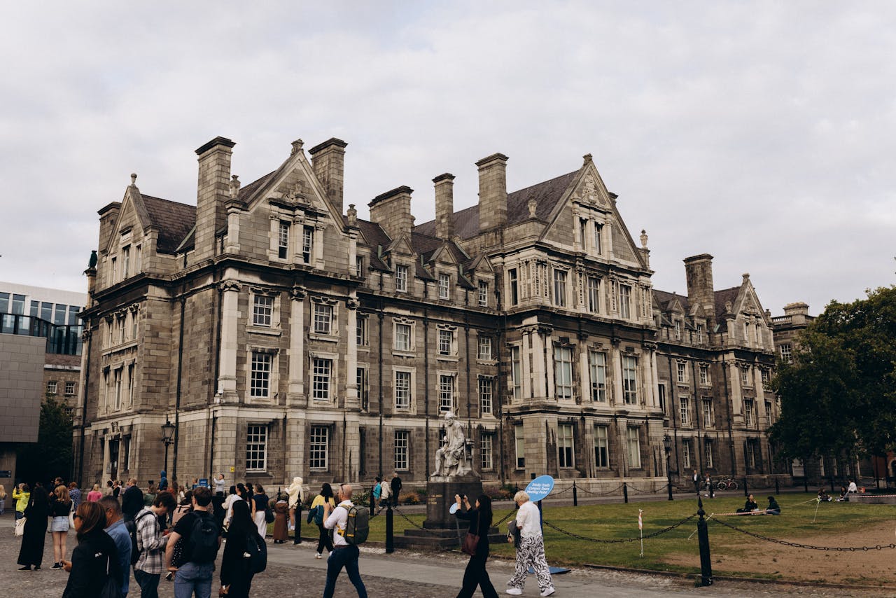 team-03 Historic architecture of Trinity College Dublin surrounded by visitors on a cloudy day.
