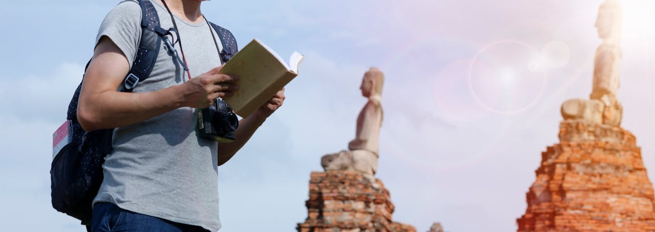 who-we-are Man with a camera and book exploring ancient ruins under bright sun.