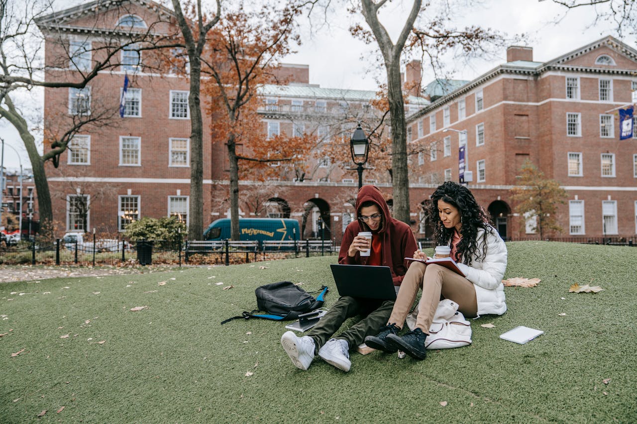 team-04 College students studying with laptops and books in a park during fall.