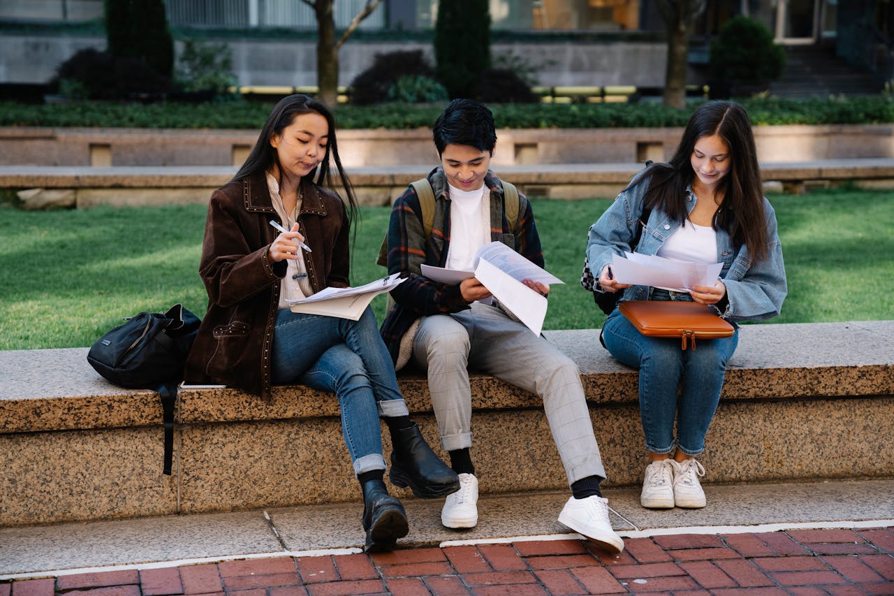 team-02 Three students studying together on a bench in a university campus setting outdoors.